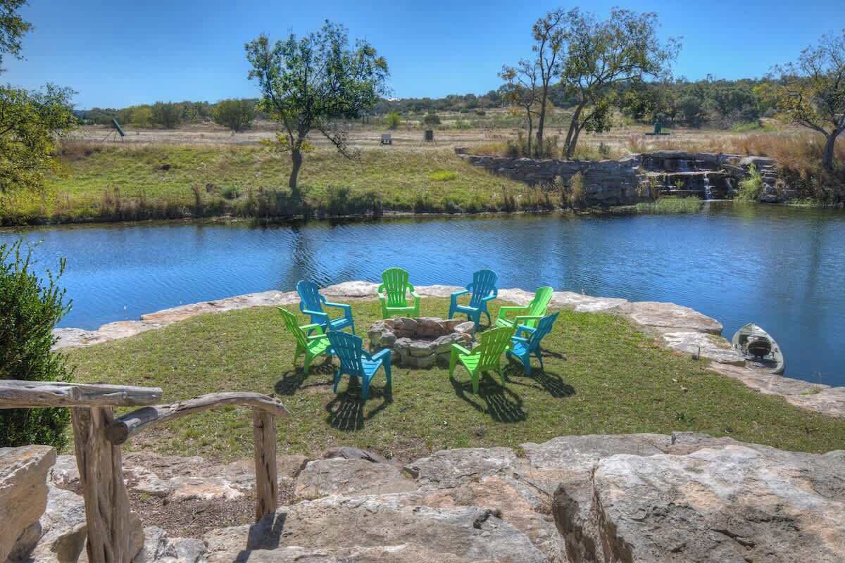 A lakeside seating area with Adirondack chairs around a fire pit.