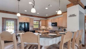 A spacious kitchen with wooden cabinets, a central island, and a dining area with chairs. - Ranch Retreat Combo With Stunning Creek View-fire Pit (Fredericksburg)