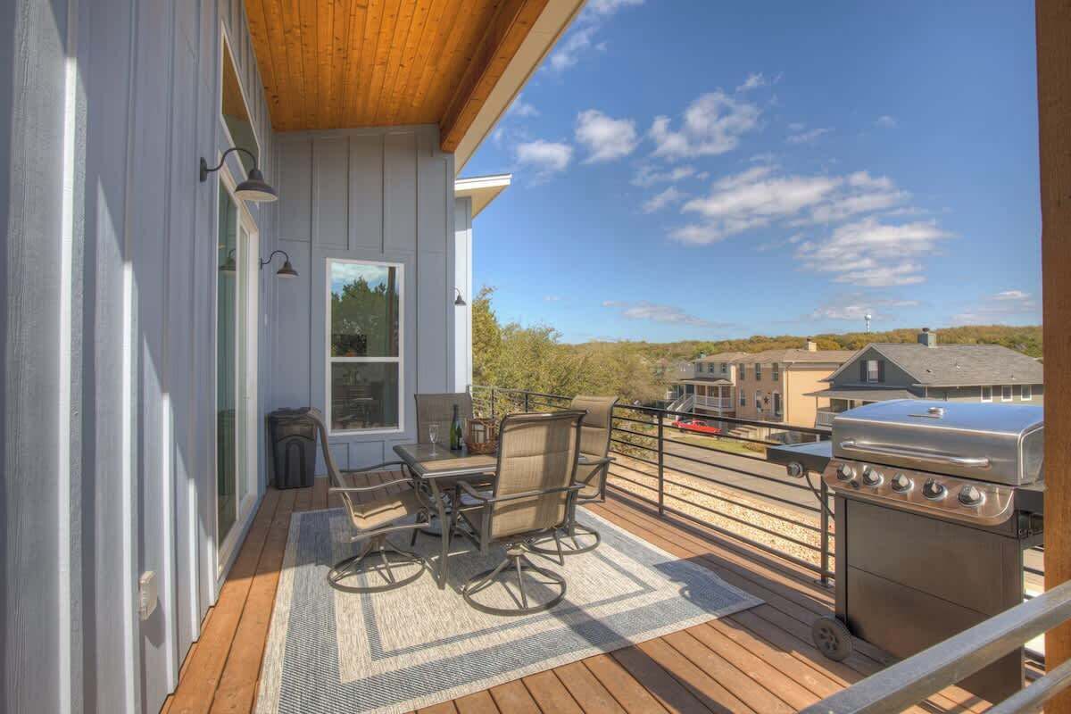 A covered outdoor deck with a grill, seating area, and a view of the surrounding landscape.