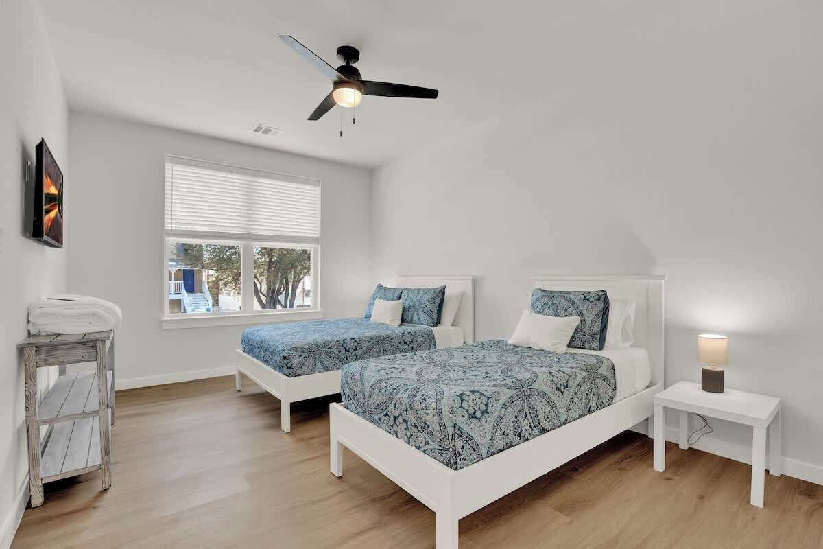 A bedroom with two beds, a ceiling fan, a window, and a bedside table with a lamp.