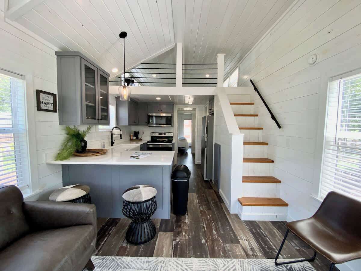 A modern kitchen with a central island, a dining area with two chairs, and a staircase leading to an upper level.