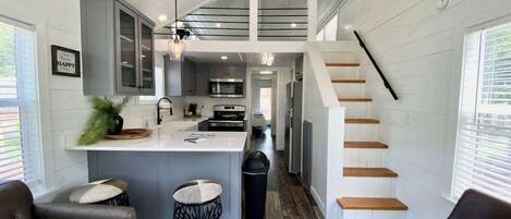 A modern kitchen with a central island, a dining area with two chairs, and a staircase leading to an upper level.