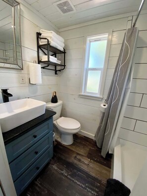 A bathroom with a white toilet, a sink with a black countertop, a mirror, and a towel rack. - Resort at Fredericksburg Unit 1 (Fredericksburg)