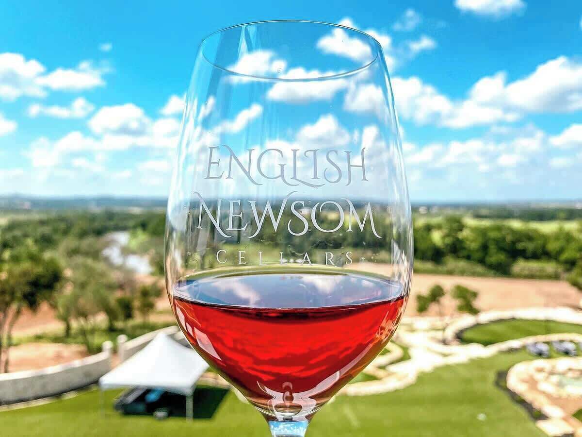 Ein Weinglas mit der Gravur 'ENGLISH NEWSOM CELLARS', vor einer Landschaftsperspektive.