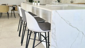 A modern kitchen with a marble countertop, bar stools, and a large window. - 22 - Villa in Cala de Mijas (La Cala de Mijas)