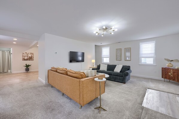A spacious living room with a large sofa, a coffee table, a TV, and a chandelier.