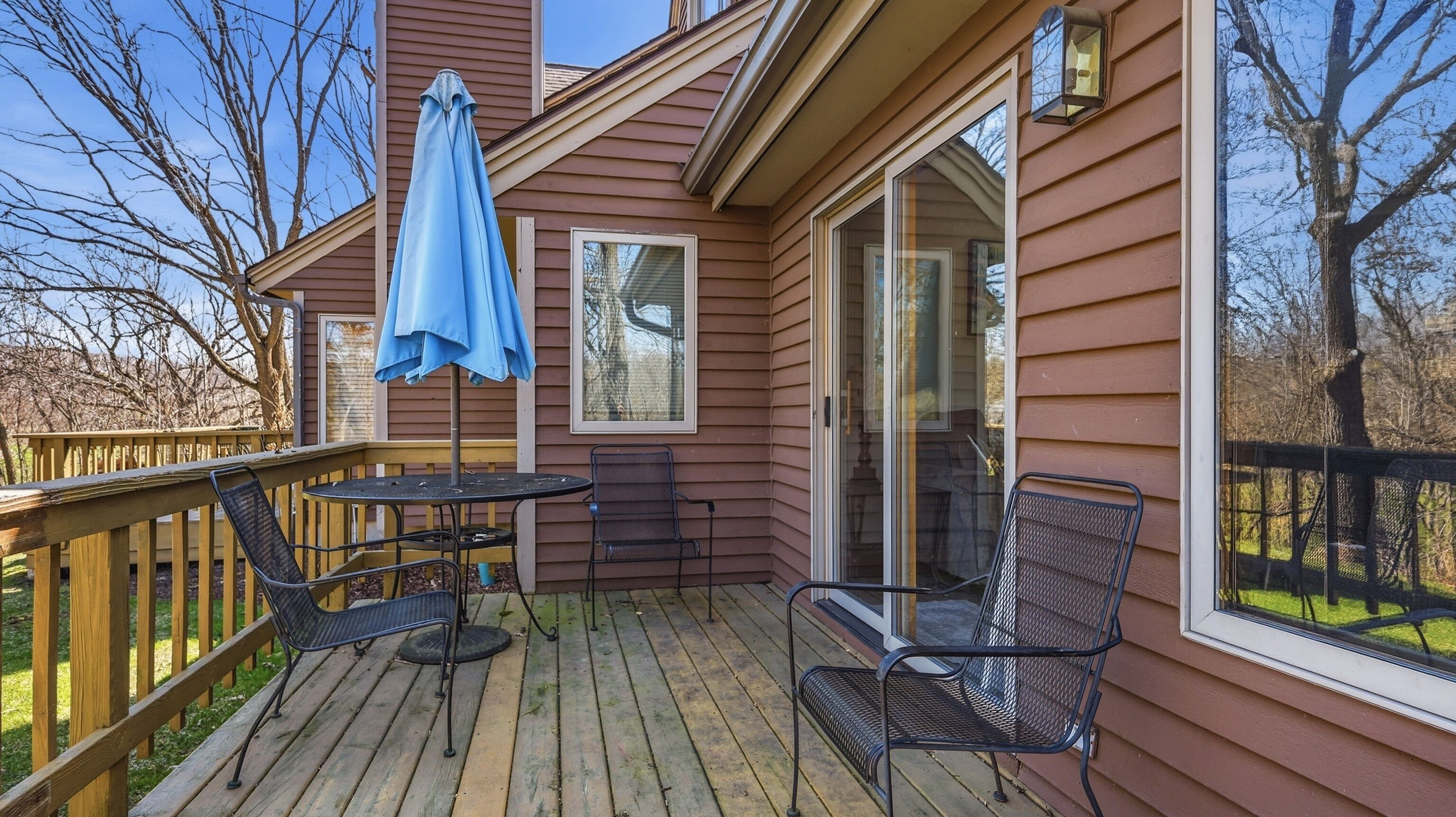 A deck with a table and chairs, a blue umbrella, and a glass door leading to a covered area.