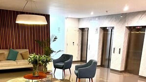 A modern lobby with a sofa, two armchairs, a coffee table, a hanging light fixture, and two elevators. - Unique Apartment. 5 Guests. 3 Bedrooms. 2 Baths. (Lima)