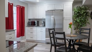 A modern kitchen with white cabinets, a stainless steel refrigerator, a microwave, and a dining area with a round table and chairs. - Spacious Basement Apartment (Eagle Mountain)