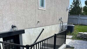 A residential building with a concrete exterior, a black metal railing, and a stone pathway leading to the entrance. - Spacious Basement Apartment (Eagle Mountain)