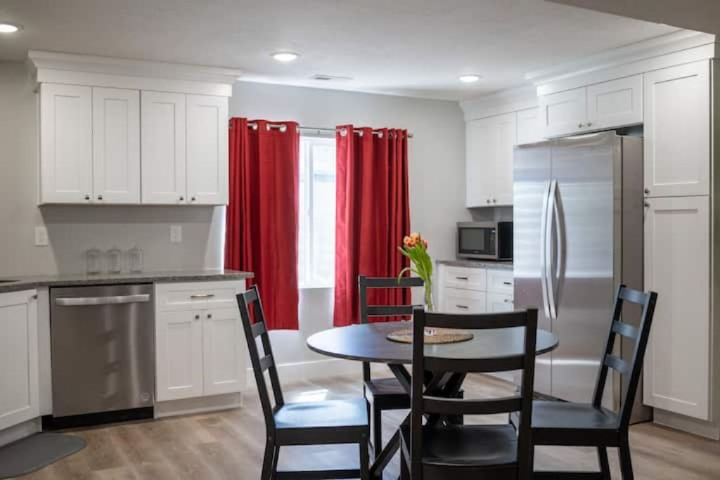 A modern kitchen with white cabinets, a stainless steel refrigerator, and a dining area with a round table and four chairs.