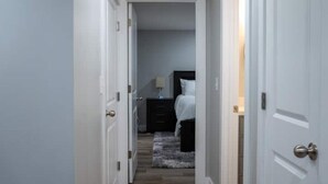 A narrow hallway leading to a bedroom with a bed, nightstand, and lamp. - Spacious Basement Apartment (Eagle Mountain)