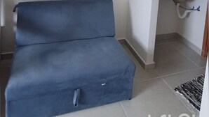 A room with a blue sofa, a tiled floor, a small bathroom with a sink and mirror, and a door leading to another room.