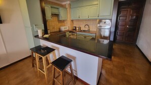 A compact kitchen with a central island, wooden stools, and light-colored cabinets. - San Marino Studio 7 (Los Cristianos)