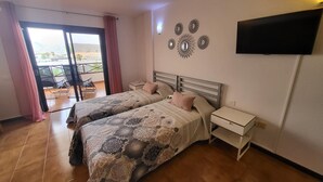 A hotel room with two beds, a balcony with a view, and a flat-screen TV mounted on the wall. - San Marino Studio 7 (Los Cristianos)