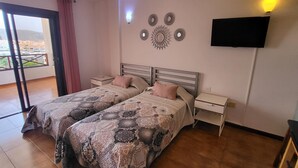 A bedroom with two beds, a TV mounted on the wall, and a balcony with a view of buildings. - San Marino Studio 7 (Los Cristianos)