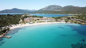 An aerial view of a coastal resort with a beach, clear turquoise waters, and mountainous background. - Porto Rotondo Vista Incantevole sul Mare e Yacht (Olbia)