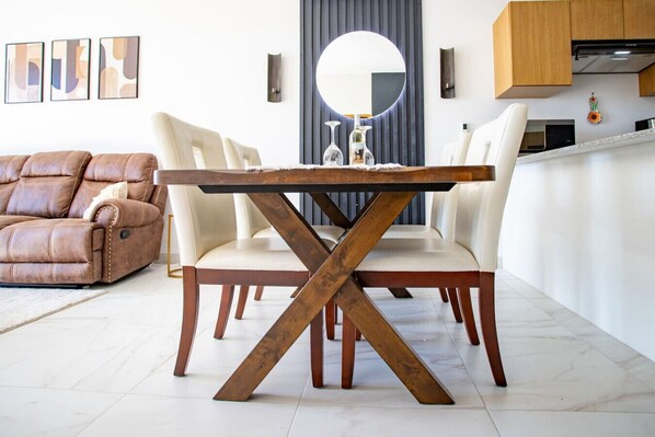 A dining area with a wooden table and chairs, a leather sofa, and a kitchen in the background. - Modern 2-Bedroom Penthouse with Pool & Private Rooftop - Sea of Cortez Views! (El tezal)