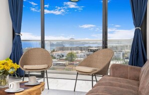 A balcony with wicker chairs, a brown sofa, and a table with a vase of yellow flowers and a white mug. - Modern 2-Bedroom Penthouse with Pool & Private Rooftop - Sea of Cortez Views! (El tezal)