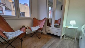 Una habitación con dos sillones de cuero, un aparador blanco, una mesita con lámpara y un espejo grande.