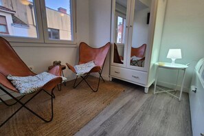 A room with two leather chairs, a white dresser, a small table with a lamp, and a large mirror.