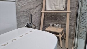 Un baño con una bañera, una escalera de madera con una toalla y artículos de aseo en una mesita.