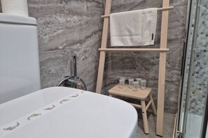 A bathroom with a bathtub, a wooden ladder with a towel, and toiletries on a small table.