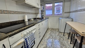 Una cocina con gabinetes blancos, estufa, microondas y una ventana que ofrece vistas a un edificio.