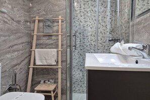 A bathroom with a marble wall, a shower with a glass door, a wooden towel rack, and a sink with a mirror.