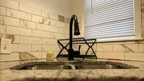 A kitchen with a marble backsplash, a black faucet, and a window with blinds. - House of Treasure, a stylish property located 8 minute from Downtown Dallas. (Dallas)