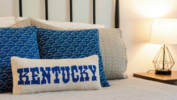 A neatly made bed with a pillow labeled "KENTUCKY," a bedside lamp, and a quilted blanket.