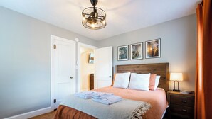 Un lit bien fait, avec une tête de lit en bois, une table de chevet avec une lampe et une porte donnant sur une autre pièce.