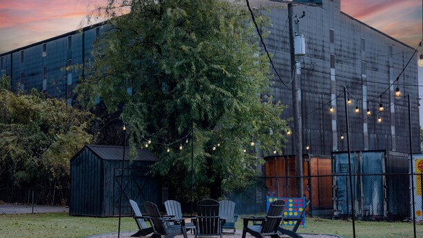 Un bâtiment avec un grand arbre devant, des sièges extérieurs avec des chaises et des guirlandes lumineuses.