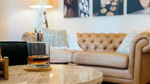 Un salon avec une table ronde, un verre de whisky, un canapé et des œuvres d’art murales.