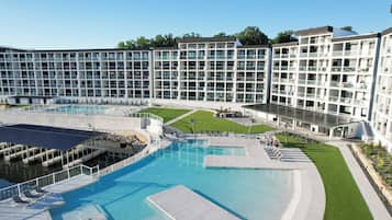 A modern hotel with a large pool area, multiple balconies, and a well-maintained lawn.