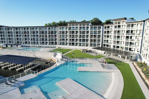 Un hotel moderno con un amplio área de piscina, varios balcones y un césped bien cuidado.