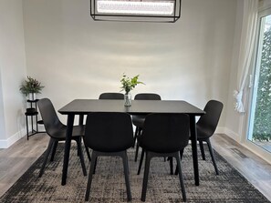 Een moderne eetruimte met een rechthoekige tafel, zes zwarte stoelen, een vaas met bloemen en een potplant.