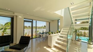 Un intérieur moderne avec un escalier en verre, un coin repas offrant une vue panoramique et une piscine à l’extérieur.