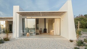 A modern building with a patio area featuring two white chairs and a small wooden stool. - Amaria (Aljezur)