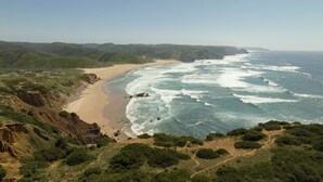 A coastal landscape with a beach, ocean waves, and green hills. - Amaria (Aljezur)