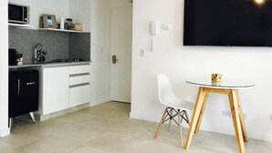A modern kitchen with white cabinets, a microwave, and a sink. There's a dining area with a glass table and two white chairs. A flat-screen TV is mounted on the wall. - PB by medrano SUITS (Buenos Aires)