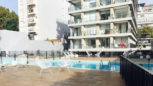 A modern apartment building with a rooftop pool area featuring white wireframe chairs and a wooden deck. - PB by medrano SUITS (Buenos Aires)