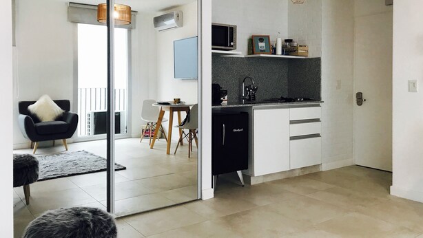 A modern kitchen with a microwave, stove, and sink. There is a dining area with a chair and table. - PB by medrano SUITS (Buenos Aires)