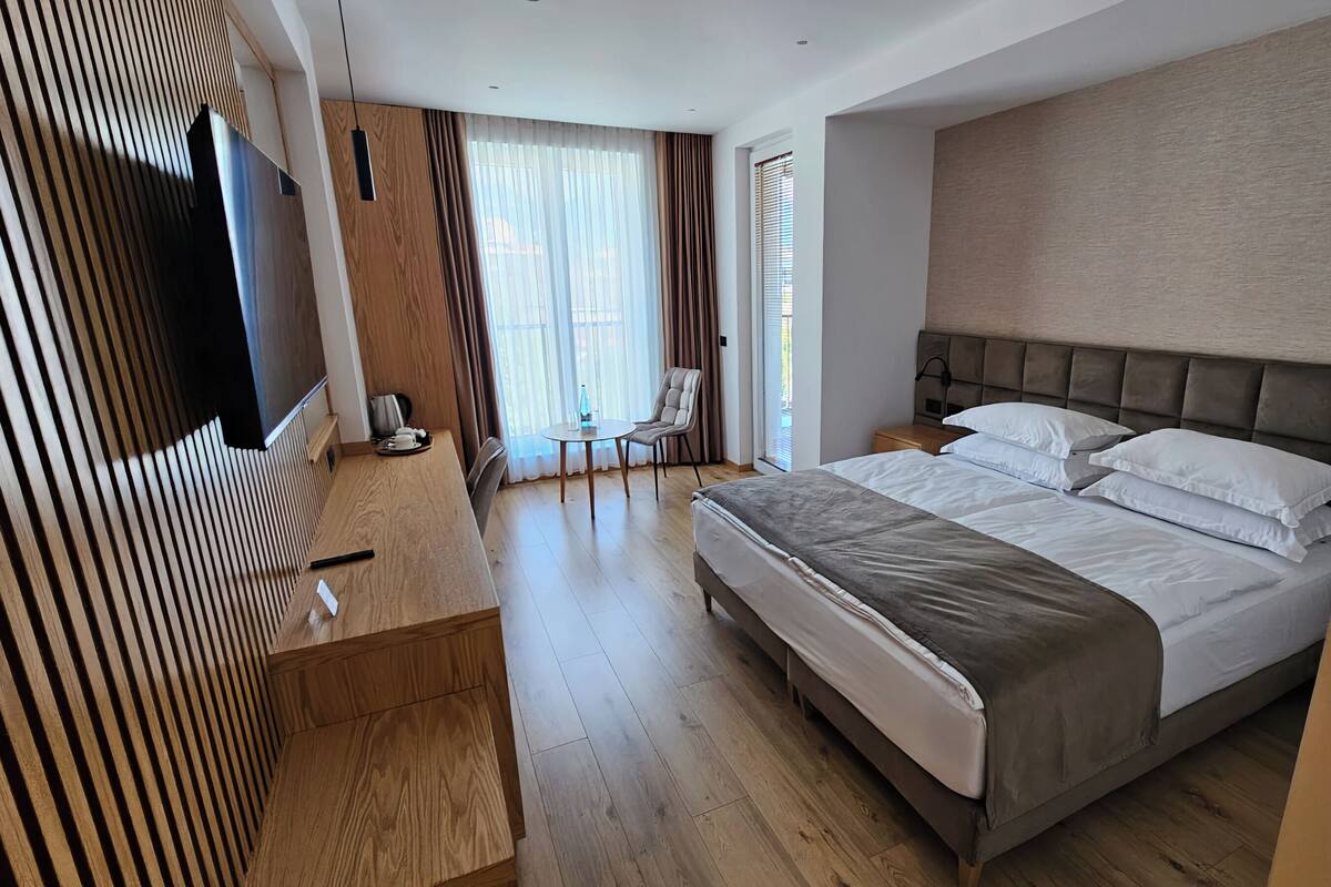 A modern hotel room with a large bed, a wooden desk, a chair, and a TV.