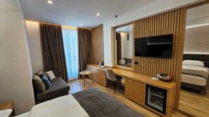 Une chambre d’hôtel moderne équipée d’un lit, d’un bureau, d’une chaise, d’une télévision et d’un mini-bar.