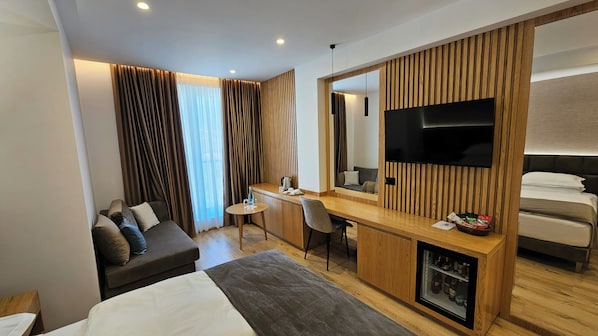 A modern hotel room with a bed, a desk, a chair, a TV, and a minibar. - SIBB Hotel (Tirana)