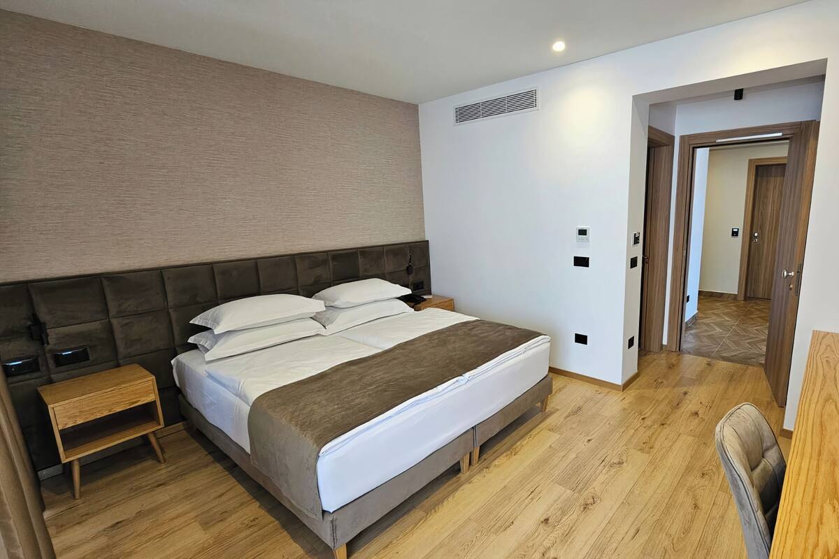 A modern hotel room with a large bed, bedside tables, a TV, and a wooden floor.