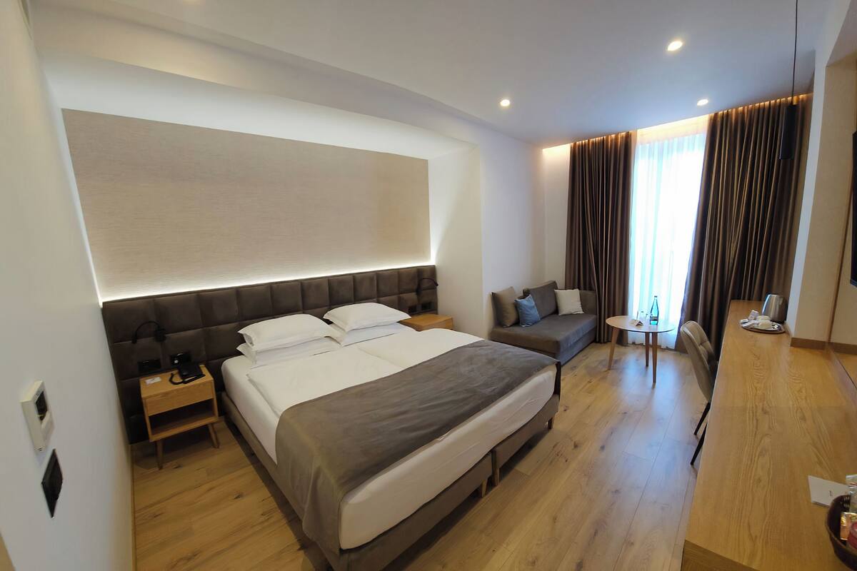 A modern hotel room with a large bed, a sofa, a small table, and a TV.