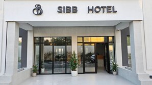 Exterior do Hotel Sibb, com entrada moderna, grandes portas de vidro e plantas em vasos.