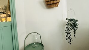 Une pièce d’angle avec un fauteuil vert, deux paniers en osier accrochés au mur et une plante suspendue.